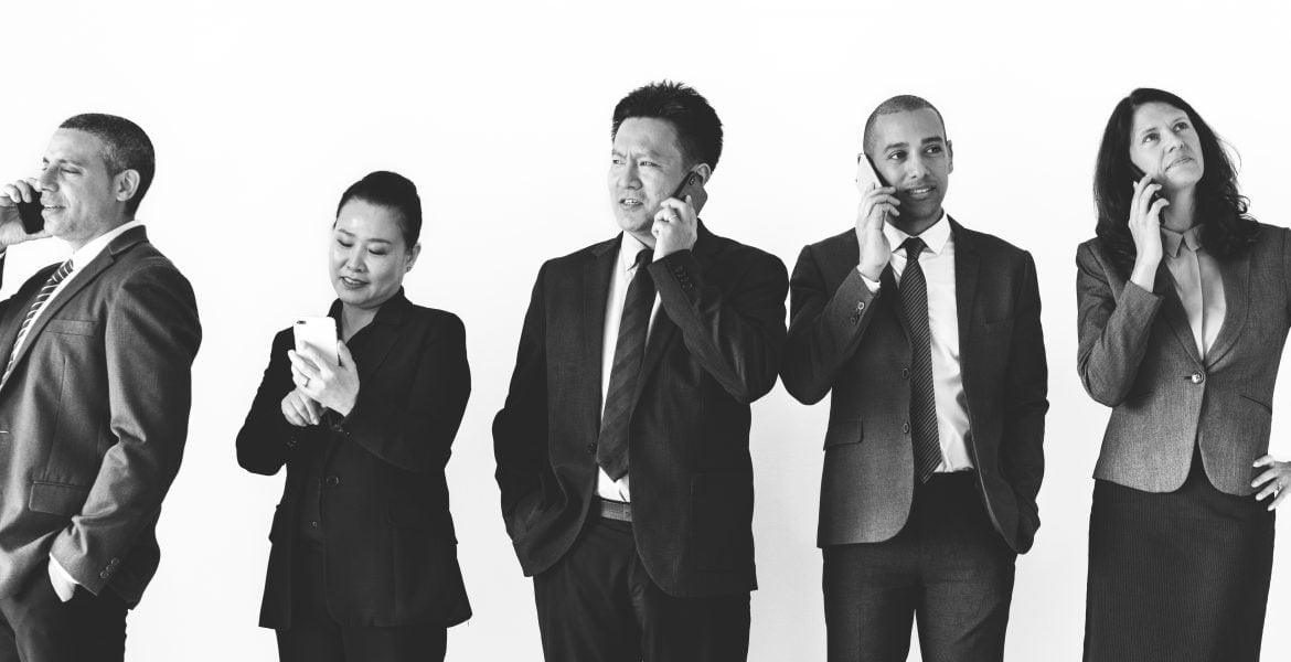 Two women and three men talking on the phone while wearing perfectly fitted suits, emphasizing the importance of suit alterations in creating a professional and polished appearance."